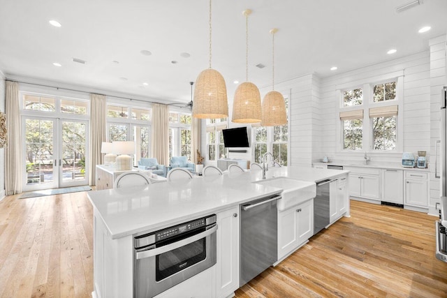 kitchen with light wood-style flooring, open floor plan, appliances with stainless steel finishes, and a center island with sink