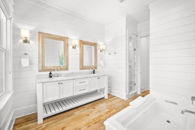 bathroom with double vanity, wood finished floors, a tub, and a sink