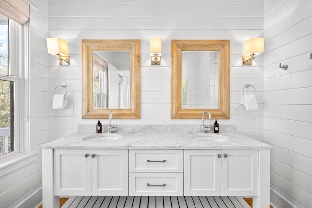 full bathroom with a sink, wood walls, and double vanity