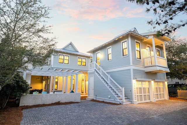 back of property featuring stairway, decorative driveway, a garage, a balcony, and a patio area