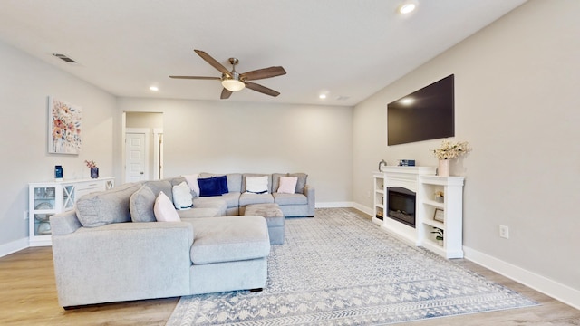 living area featuring recessed lighting, visible vents, baseboards, light wood-type flooring, and a glass covered fireplace