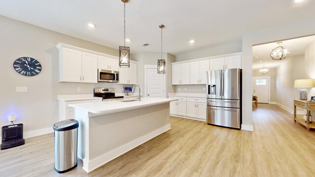 kitchen featuring a center island with sink, light wood finished floors, stainless steel appliances, light countertops, and white cabinets