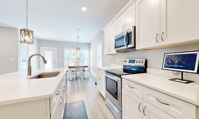 kitchen with a sink, white cabinetry, light countertops, appliances with stainless steel finishes, and light wood finished floors