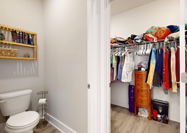 bathroom with toilet, a spacious closet, baseboards, and wood finished floors