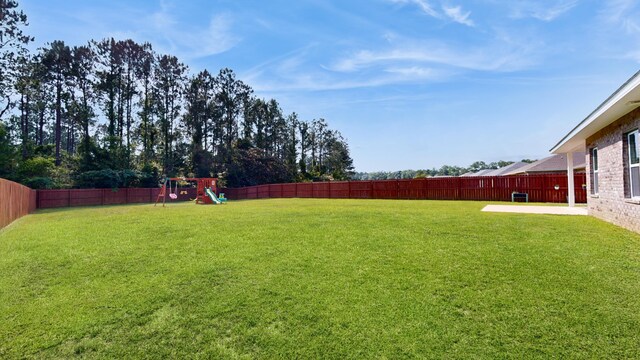 view of yard featuring a fenced backyard, a playground, and a patio