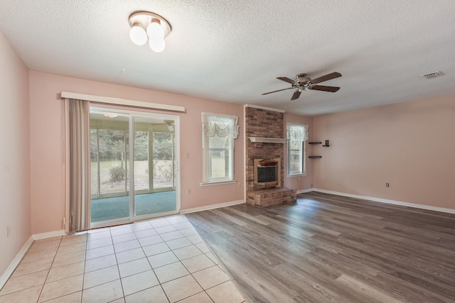 unfurnished living room featuring light wood finished floors, visible vents, ceiling fan, a textured ceiling, and a fireplace