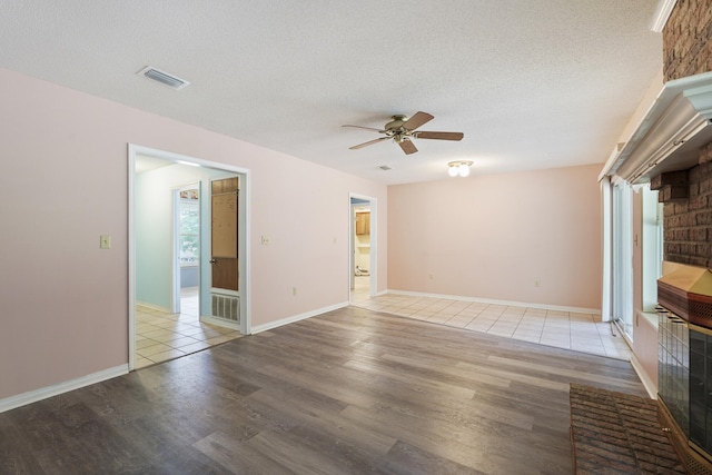 unfurnished living room featuring visible vents, a ceiling fan, a textured ceiling, wood finished floors, and baseboards