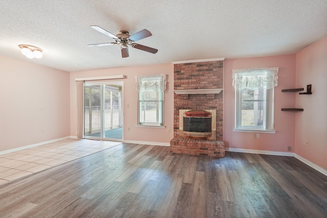 unfurnished living room with a textured ceiling, a fireplace, baseboards, and wood finished floors