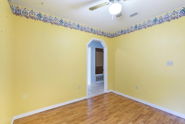 empty room featuring arched walkways, visible vents, light wood-style floors, ceiling fan, and baseboards