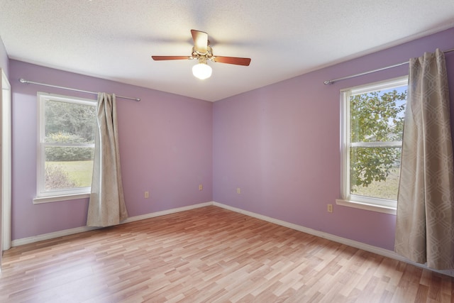 spare room with light wood finished floors, baseboards, and a textured ceiling