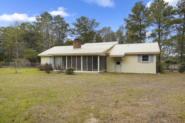 back of house with a yard, a chimney, a sunroom, metal roof, and fence