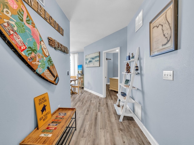 hall featuring light wood-style floors, visible vents, and baseboards