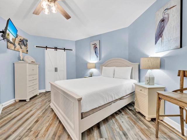 bedroom with light wood-style floors, ceiling fan, baseboards, and a barn door