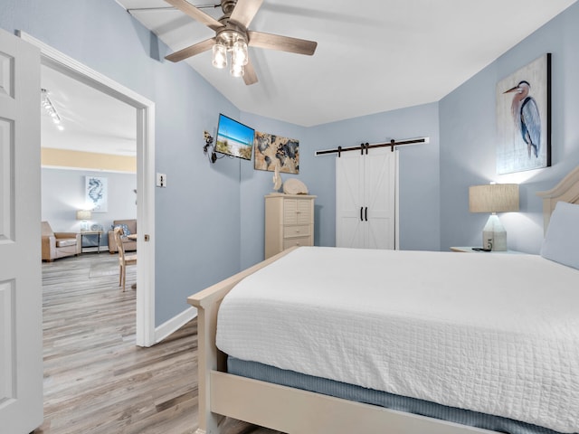 bedroom with a barn door, wood finished floors, a ceiling fan, and baseboards