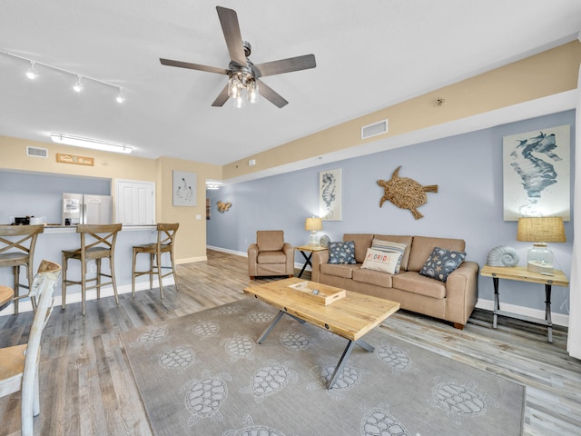 living area featuring baseboards, visible vents, ceiling fan, and wood finished floors