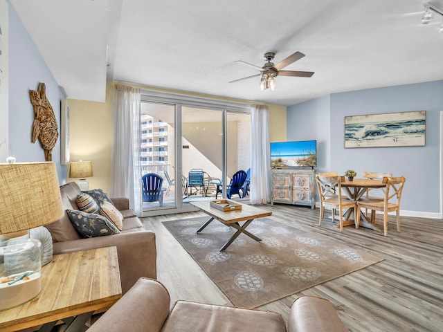 living area with a ceiling fan, baseboards, and wood finished floors