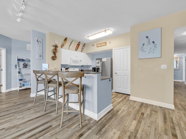 kitchen featuring white microwave, freestanding refrigerator, a peninsula, light wood-type flooring, and white cabinetry