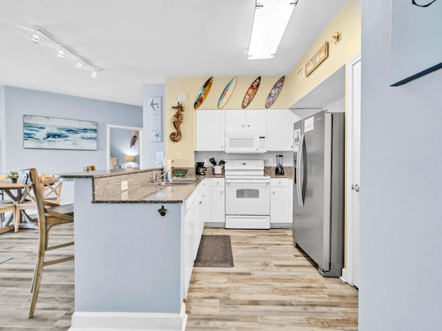 kitchen with light wood-style floors, white cabinetry, dark stone counters, white appliances, and a peninsula