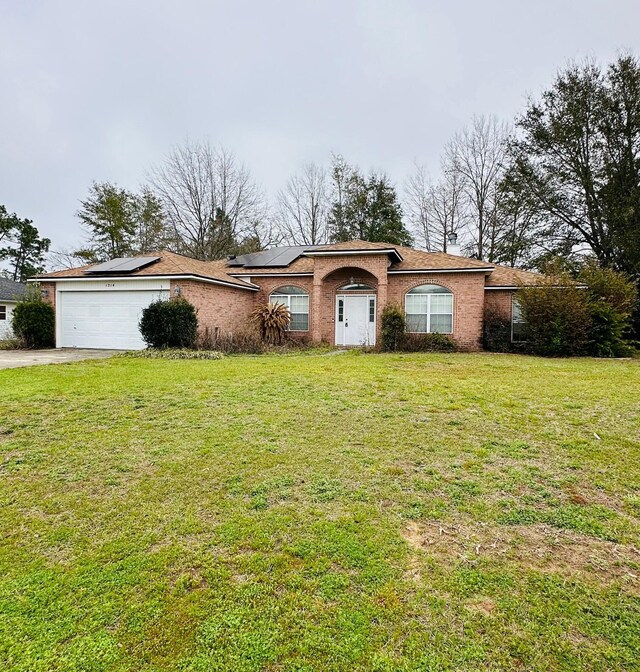 ranch-style house featuring brick siding, solar panels, an attached garage, and a front yard