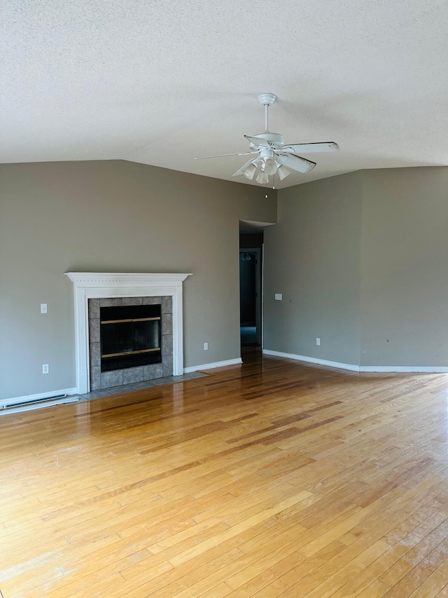 unfurnished living room with ceiling fan, vaulted ceiling, light wood-style flooring, a fireplace, and a textured ceiling