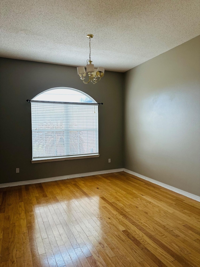 spare room with a notable chandelier, baseboards, and wood-type flooring