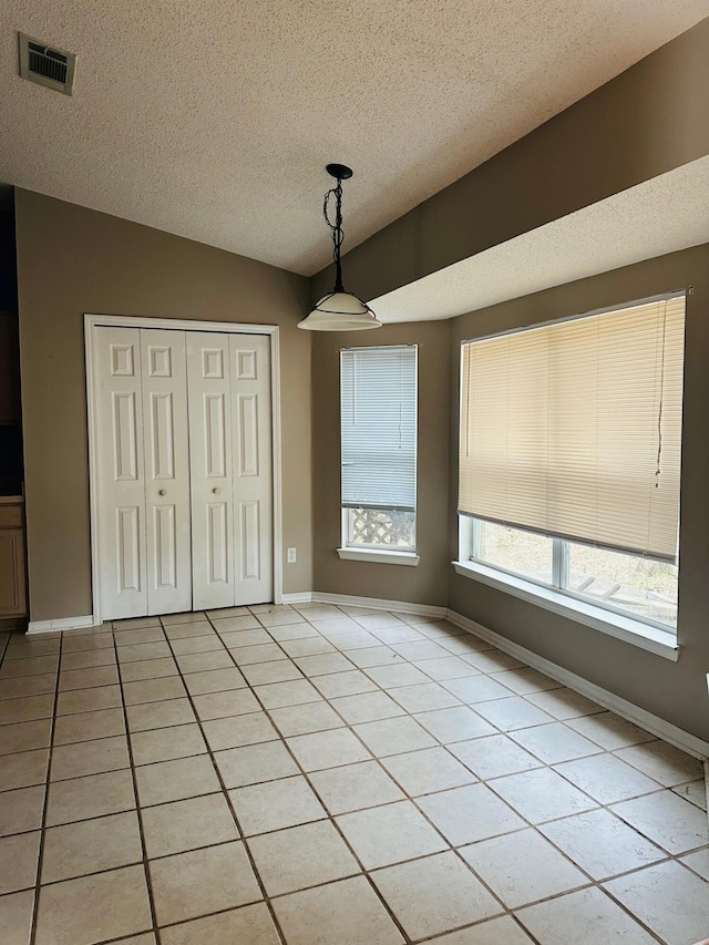 unfurnished dining area with baseboards, visible vents, lofted ceiling, light tile patterned flooring, and a textured ceiling