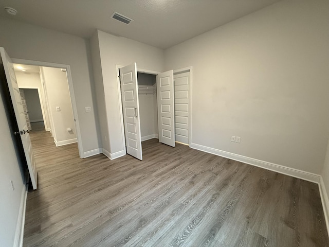 unfurnished bedroom with a closet, visible vents, baseboards, and wood finished floors