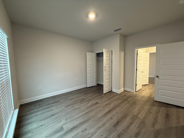 unfurnished bedroom featuring visible vents, baseboards, a closet, and dark wood-style flooring