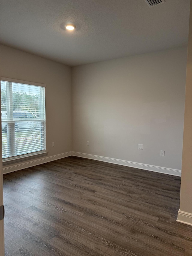 empty room with visible vents, a textured ceiling, baseboards, and dark wood-style flooring