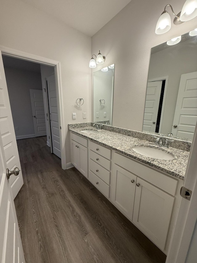 full bath with double vanity, wood finished floors, baseboards, and a sink