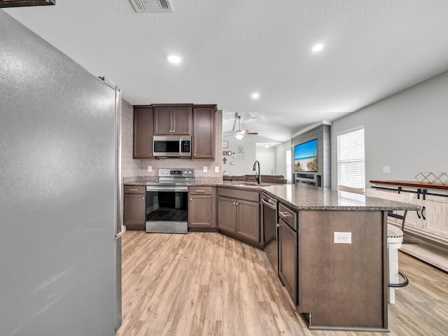 kitchen featuring light wood finished floors, visible vents, appliances with stainless steel finishes, a sink, and a peninsula