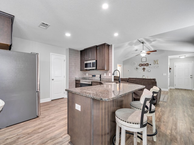 kitchen featuring a breakfast bar area, stone counters, a sink, visible vents, and appliances with stainless steel finishes