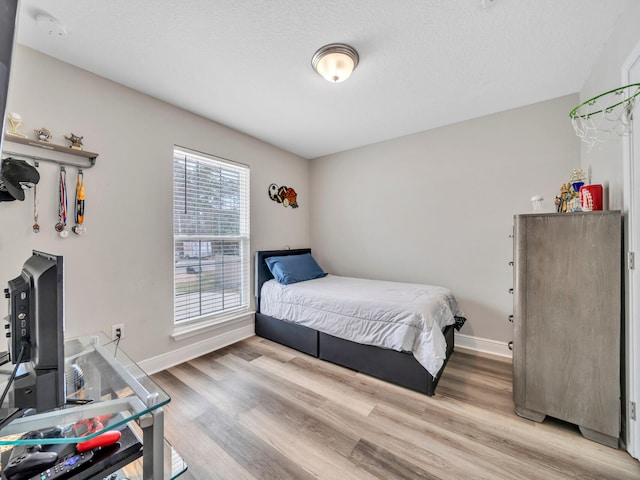 bedroom featuring light wood-type flooring, baseboards, and a textured ceiling