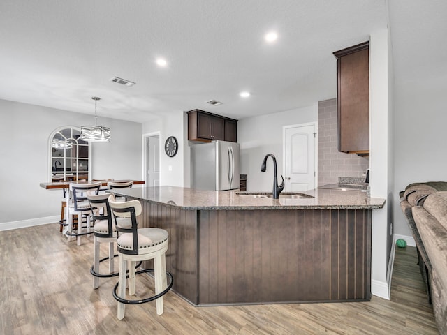 kitchen featuring visible vents, light wood-style floors, freestanding refrigerator, a sink, and dark stone countertops