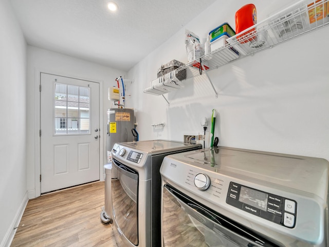 washroom with laundry area, baseboards, electric water heater, washer and dryer, and light wood-type flooring