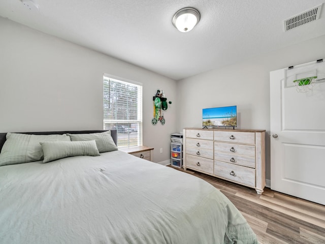 bedroom featuring a textured ceiling, wood finished floors, visible vents, and baseboards