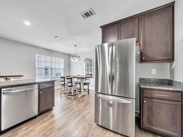 kitchen with stainless steel appliances, dark brown cabinets, light wood-type flooring, and visible vents