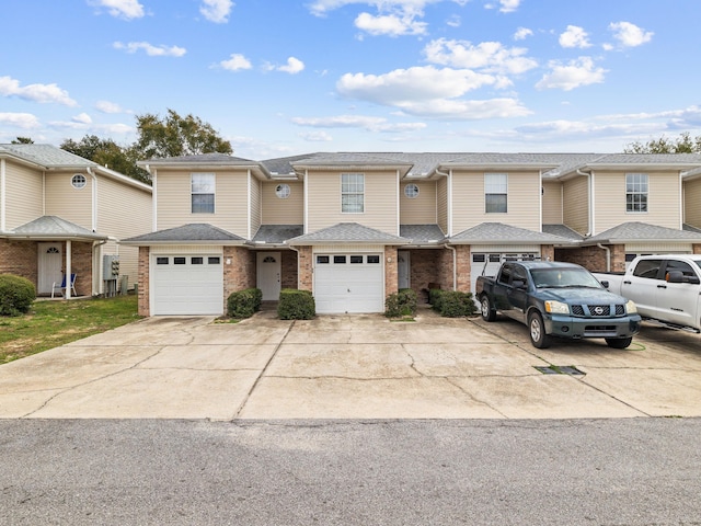 townhome / multi-family property with brick siding, an attached garage, driveway, and roof with shingles