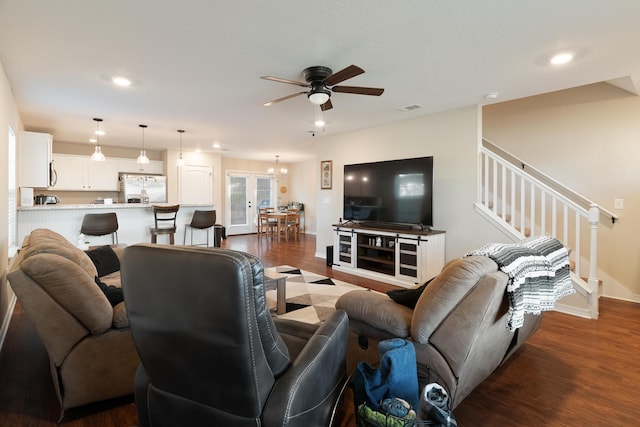 living area with visible vents, ceiling fan with notable chandelier, dark wood-type flooring, and stairway