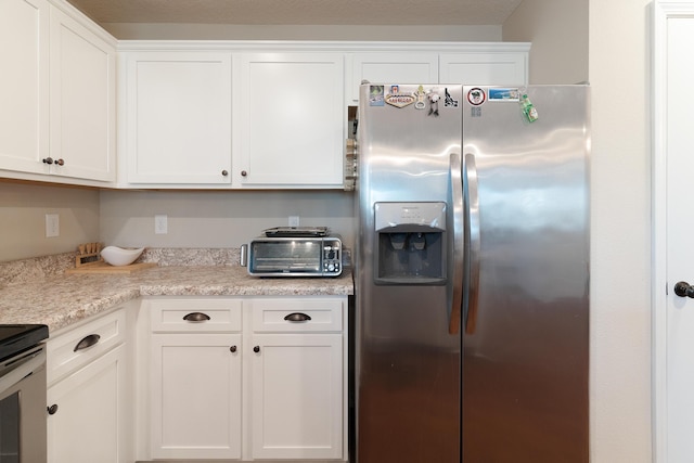 kitchen with stove, stainless steel fridge, white cabinetry, and light countertops