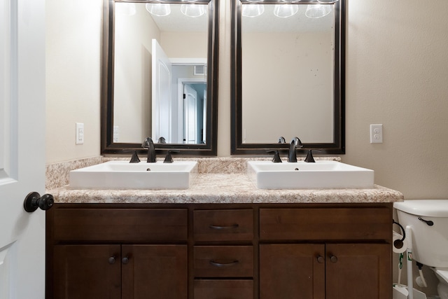 bathroom with double vanity, toilet, and a sink