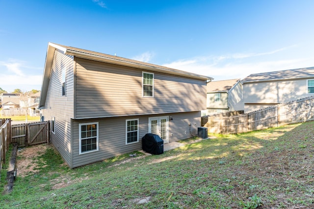 rear view of property with a gate, a yard, a fenced backyard, central AC, and french doors