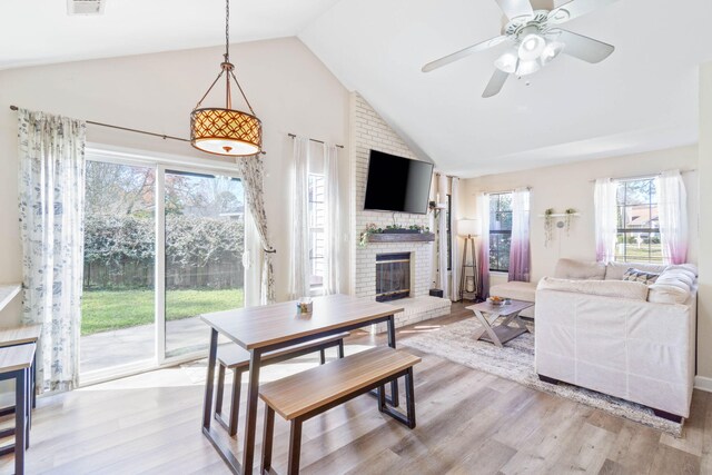 living area featuring lofted ceiling, visible vents, light wood-style floors, a brick fireplace, and ceiling fan