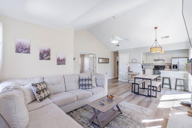 living area with visible vents, baseboards, ceiling fan, light wood-type flooring, and high vaulted ceiling