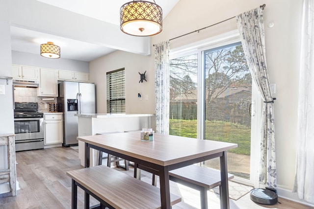 dining area with light wood-style floors and vaulted ceiling