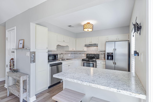 kitchen featuring under cabinet range hood, a peninsula, visible vents, appliances with stainless steel finishes, and backsplash