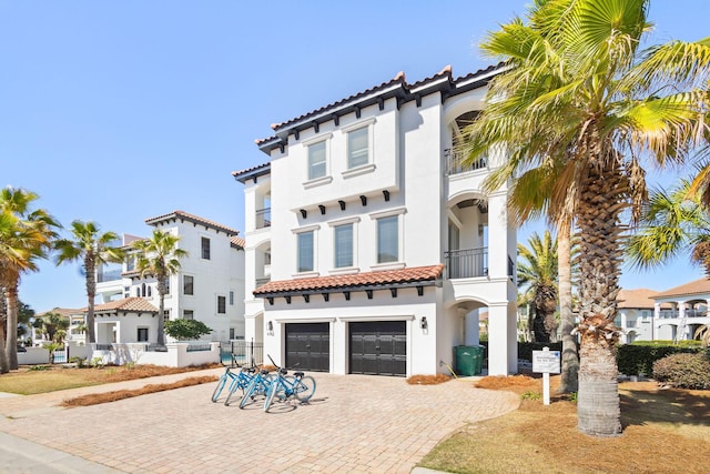 mediterranean / spanish home featuring decorative driveway, a tile roof, stucco siding, an attached garage, and fence