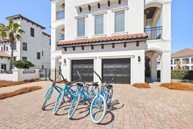 view of front of house with decorative driveway, stucco siding, fence, a garage, and a tiled roof