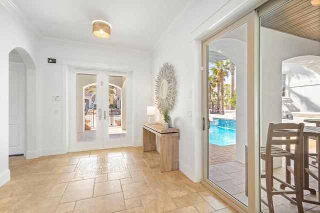 doorway with arched walkways, french doors, crown molding, stone tile flooring, and baseboards