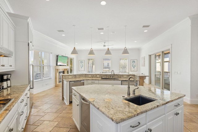 kitchen with an island with sink, stone tile floors, crown molding, and a sink